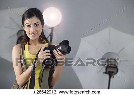 Stock Image - Portrait of beautiful photographer smiling with digital camera in studio . Fotosearch