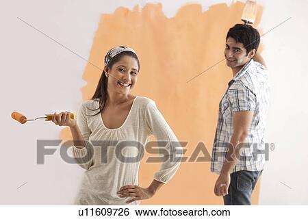 Stock Photograph - Portrait of beautiful woman smiling with man painting wall in background . Fotosearch
