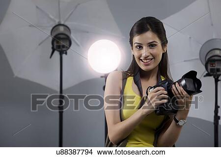 Picture - Portrait of beautiful young photographer holding camera in her studio . Fotosearch