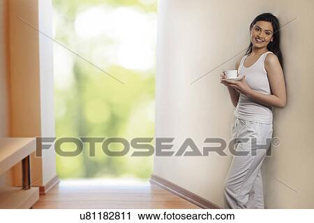 Portrait of beautiful young woman leaning on wall while holding cup of coffee View Large Photo Image Stock Image - Portrait of beautiful young woman leaning on wall while holding cup of coffee . Fotosearch