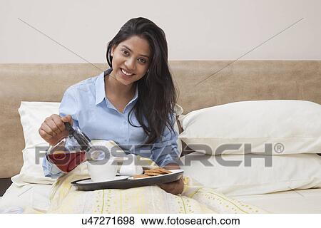 Portrait of beautiful young woman pouring tea in cup while sitting in bed View Large Photo Image Stock Photo - Portrait of beautiful young woman pouring tea in cup while sitting in bed . Fotosearch