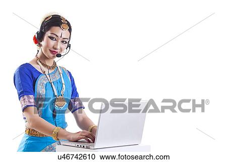 Stock Image - Portrait of Bharatanatyam dancer wearing headset while using laptop over white background. Fotosearch