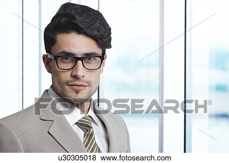 Stock Photo - Portrait of confident businessman wearing glasses in office. Fotosearch