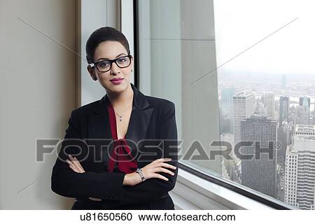 Stock Image - Portrait of confident businesswoman standing by window in office. Fotosearch