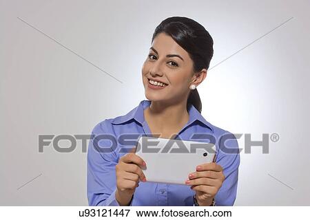 Stock Photo - Portrait of confident businesswoman holding digital tablet over gray background. Fotosearch