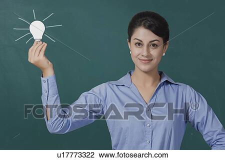 Portrait of confident young businesswoman holding light bulb against green board at office View Large Photo Image Stock Image - Portrait of confident young businesswoman holding light bulb against green board at office. Fotosearch