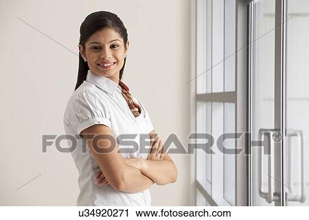 Stock Image - Portrait of confident young businesswoman smiling with arms crossed . Fotosearch