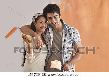 Portrait of cute young couple smiling while painting their house View Large Photo Image Stock Photo - Portrait of cute young couple smiling while painting their house . Fotosearch