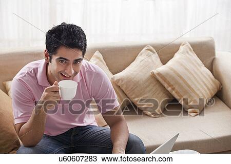Stock Image - Portrait of handsome man drinking coffee with laptop . Fotosearch
