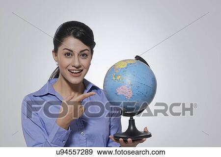 Portrait of happy businesswoman pointing at globe against gray background View Large Photo Image Stock Photo - Portrait of happy businesswoman pointing at globe against gray background. Fotosearch