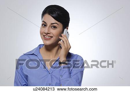 Stock Image - Portrait of happy businesswoman using mobile phone over gray background. Fotosearch
