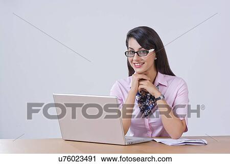 Stock Image - Portrait of happy businesswoman with laptop at office desk. Fotosearch
