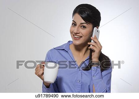 Stock Image - Portrait of happy businesswoman with coffee mug using phone against gray background. Fotosearch