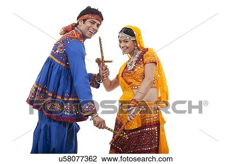 Stock Image - Portrait of happy couple performing Dandiya Raas against white background. Fotosearch