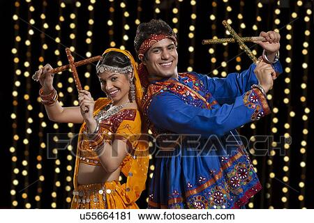 Portrait of happy Indian couple performing Dandiya Raas against neon lights View Large Photo Image Stock Image - Portrait of happy Indian couple performing Dandiya Raas against neon lights. Fotosearch
