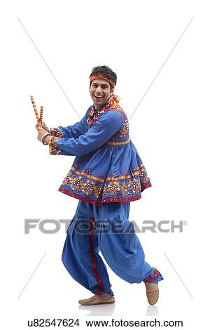 Picture - Portrait of happy man in kedia and dhoti performing Dandiya Rass isolated over white background. Fotosearch