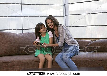 Stock Image - Portrait of happy mother and daughter playing video game together at home . Fotosearch
