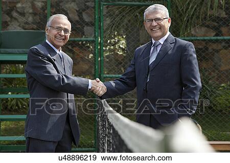Portrait of happy senior male professionals shaking hands over tennis net in court View Large Photo Image Stock Photo - Portrait of happy senior male professionals shaking hands over tennis net in court . Fotosearch