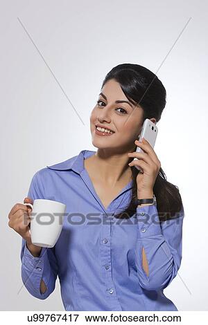 Portrait of happy young businesswoman with coffee mug answering phone over gray background View Large Photo Image Stock Photo - Portrait of happy young businesswoman with coffee mug answering phone over gray background. Fotosearch