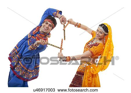 Stock Image - Portrait of happy young couple in traditional wear performing Dandiya Raas against white background. Fotosearch