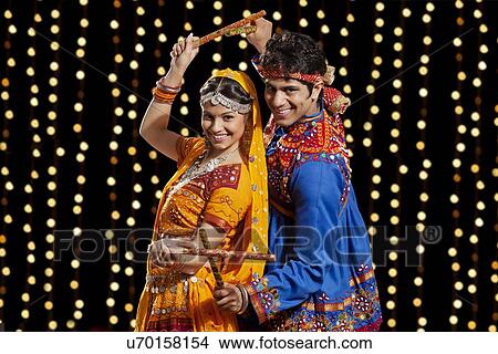 Picture - Portrait of happy young couple performing Dandiya Raas against neon lights. Fotosearch