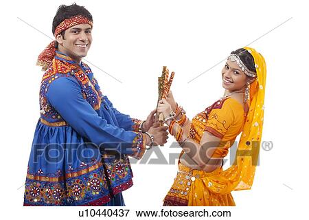Portrait of happy young couple performing Dandiya Raas over white background View Large Photo Image Stock Photo - Portrait of happy young couple performing Dandiya Raas over white background. Fotosearch