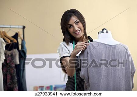 Stock Image - Portrait of happy young female designer fixing dress on mannequin . Fotosearch