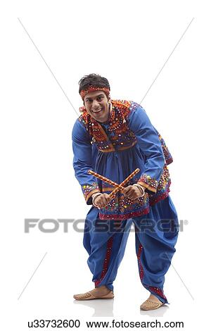 Stock Image - Portrait of happy young man in kedia and dhoti performing Dandiya Rass over white background. Fotosearch
