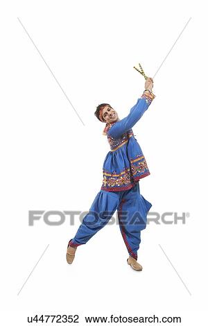 Stock Image - Portrait of happy young man in traditional clothes performing Dandiya Raas against white background. Fotosearch
