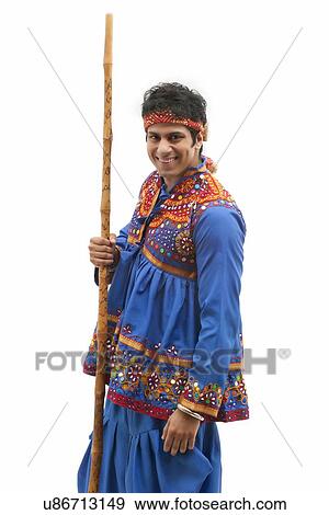 Portrait of happy young man in traditional wear holding stick against white background View Large Photo Image Stock Photo - Portrait of happy young man in traditional wear holding stick against white background. Fotosearch