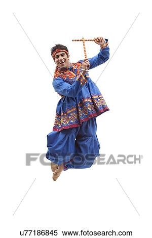 Stock Photography - Portrait of happy young man in traditional wear jumping in mid air as he performs Dandiya Raas over white background. Fotosearch