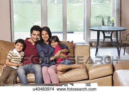Portrait of happy young parents sitting with children on sofa at home View Large Photo Image Picture - Portrait of happy young parents sitting with children on sofa at home . Fotosearch