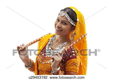 Portrait of happy young woman in traditional wear holding dandiyas isolated over white background View Large Photo Image Stock Image - Portrait of happy young woman in traditional wear holding dandiyas isolated over white background. Fotosearch