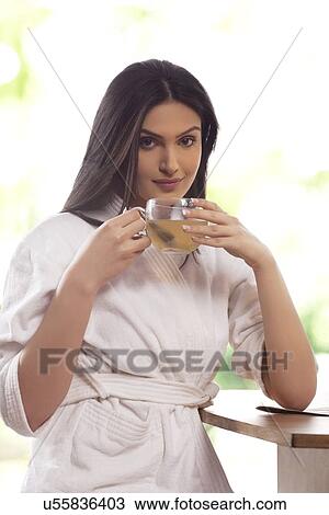 Stock Image - Portrait of happy young woman in bathrobe drinking tea . Fotosearch