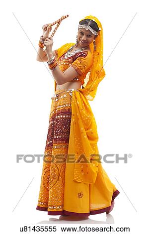 Stock Photography - Portrait of happy young woman in chaniya choli performing Dandiya Raas against white background. Fotosearch