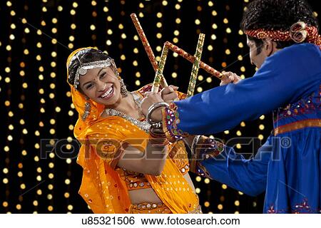 Portrait of happy young woman performing Dandiya Raas with man against neon lights View Large Photo Image Stock Photograph - Portrait of happy young woman performing Dandiya Raas with man against neon lights. Fotosearch