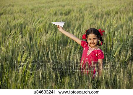 Stock Image - Portrait of little girl playing with a paper aero plane in wheat field . Fotosearch