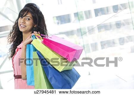 Portrait of pretty young woman smiling while carrying shopping bags View Large Photo Image Stock Image - Portrait of pretty young woman smiling while carrying shopping bags . Fotosearch
