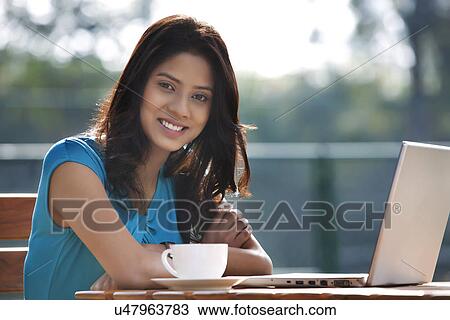 Portrait of pretty young woman smiling while sitting at table with laptop and cup of coffee View Large Photo Image Stock Image - Portrait of pretty young woman smiling while sitting at table with laptop and cup of coffee . Fotosearch