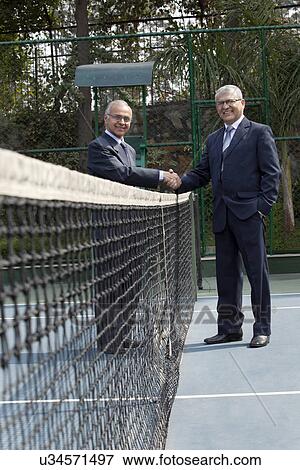 Stock Photo - Portrait of senior professionals shaking hands over a tennis net in court . Fotosearch