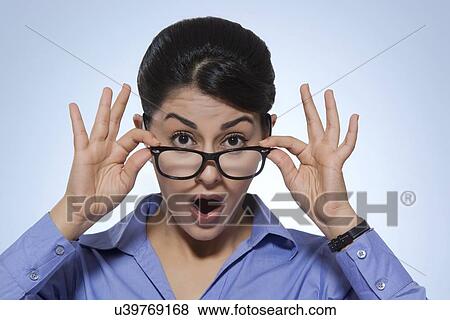 Stock Photo - Portrait of shocked businesswoman looking over glasses against blue background. Fotosearch