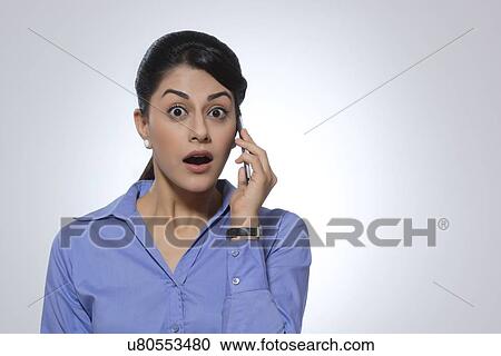 Portrait of shocked businesswoman using mobile phone against gray background View Large Photo Image Stock Image - Portrait of shocked businesswoman using mobile phone against gray background. Fotosearch
