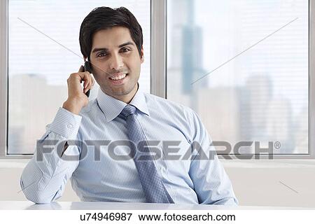 Portrait of smiling businessman speaking on phone call at office View Large Photo Image Stock Photo - Portrait of smiling businessman speaking on phone call at office . Fotosearch