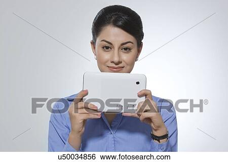 Stock Photograph - Portrait of smiling businesswoman holding digital tablet against gray background. Fotosearch