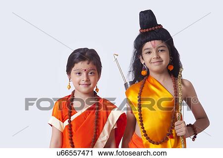 Stock Image - Portrait of smiling children dressed as Ram and Sita against white background. Fotosearch