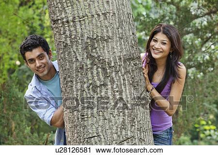 Stock Image - Portrait of smiling college students behind tree . Fotosearch