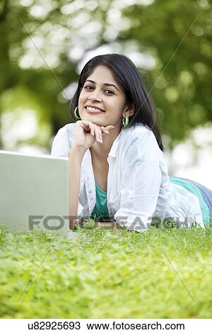 Portrait of smiling woman using laptop while lying on grass View Large Photo Image Stock Image - Portrait of smiling woman using laptop while lying on grass . Fotosearch