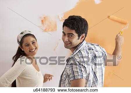 Portrait of smiling young man with woman applying orange paint on wall View Large Photo Image Stock Image - Portrait of smiling young man with woman applying orange paint on wall . Fotosearch