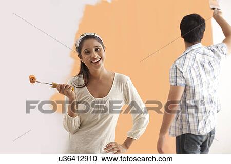 Portrait of smiling young woman with man painting wall in background View Large Photo Image Stock Image - Portrait of smiling young woman with man painting wall in background . Fotosearch