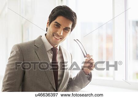Stock Photo - Portrait of successful businessman smiling while holding glasses . Fotosearch